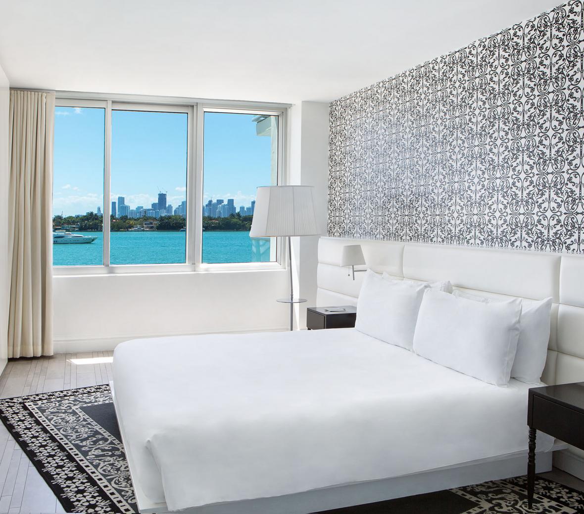 A hotel room bed next to a seaside window.