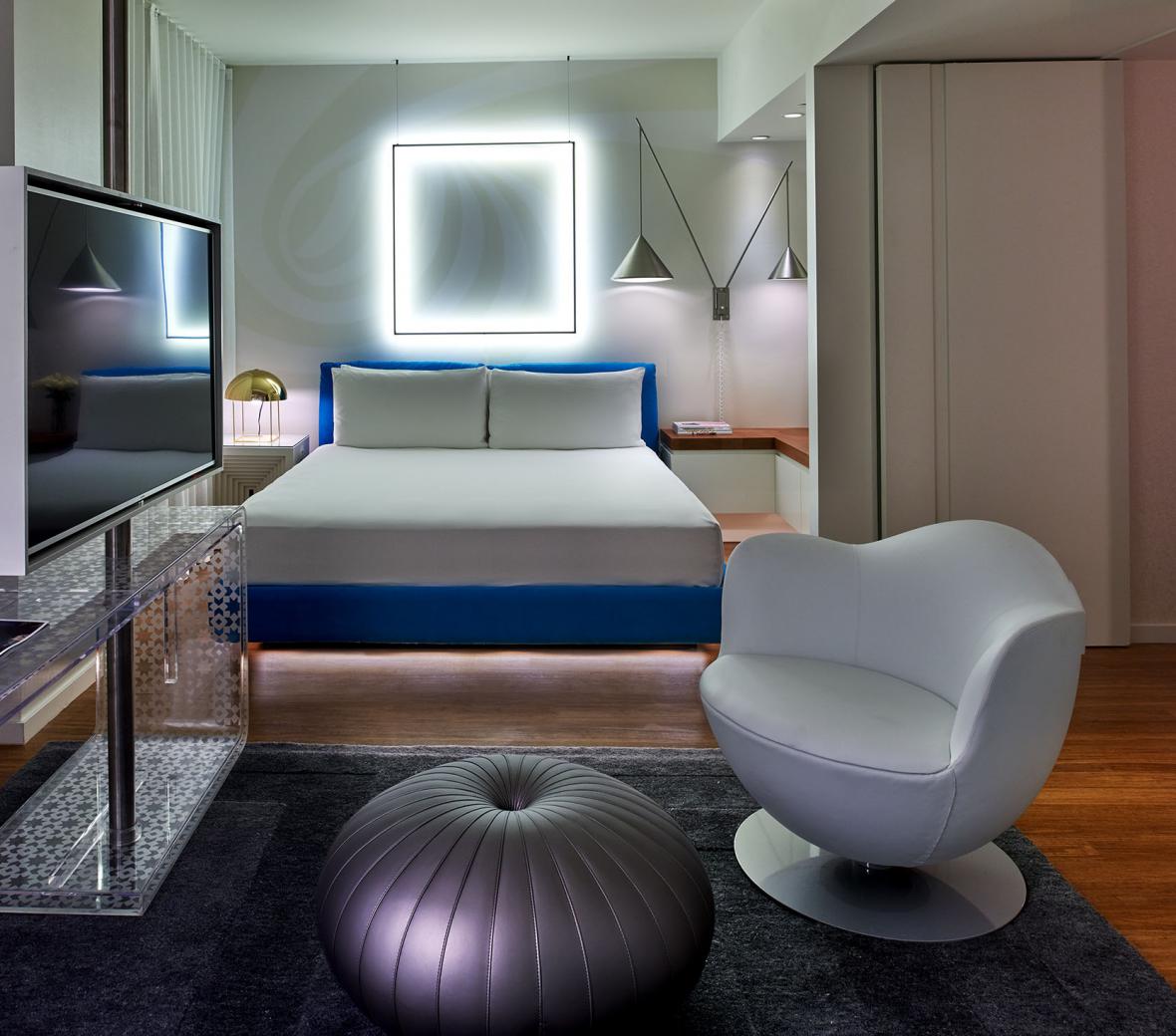 A hotel room with a square light behind the bed and a chair in the foreground.