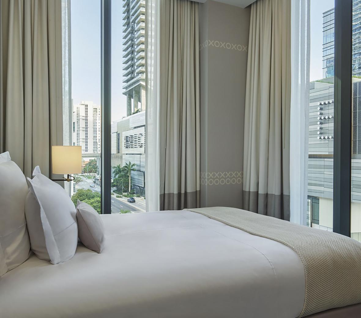 hotel bed by large windows overlooking the city