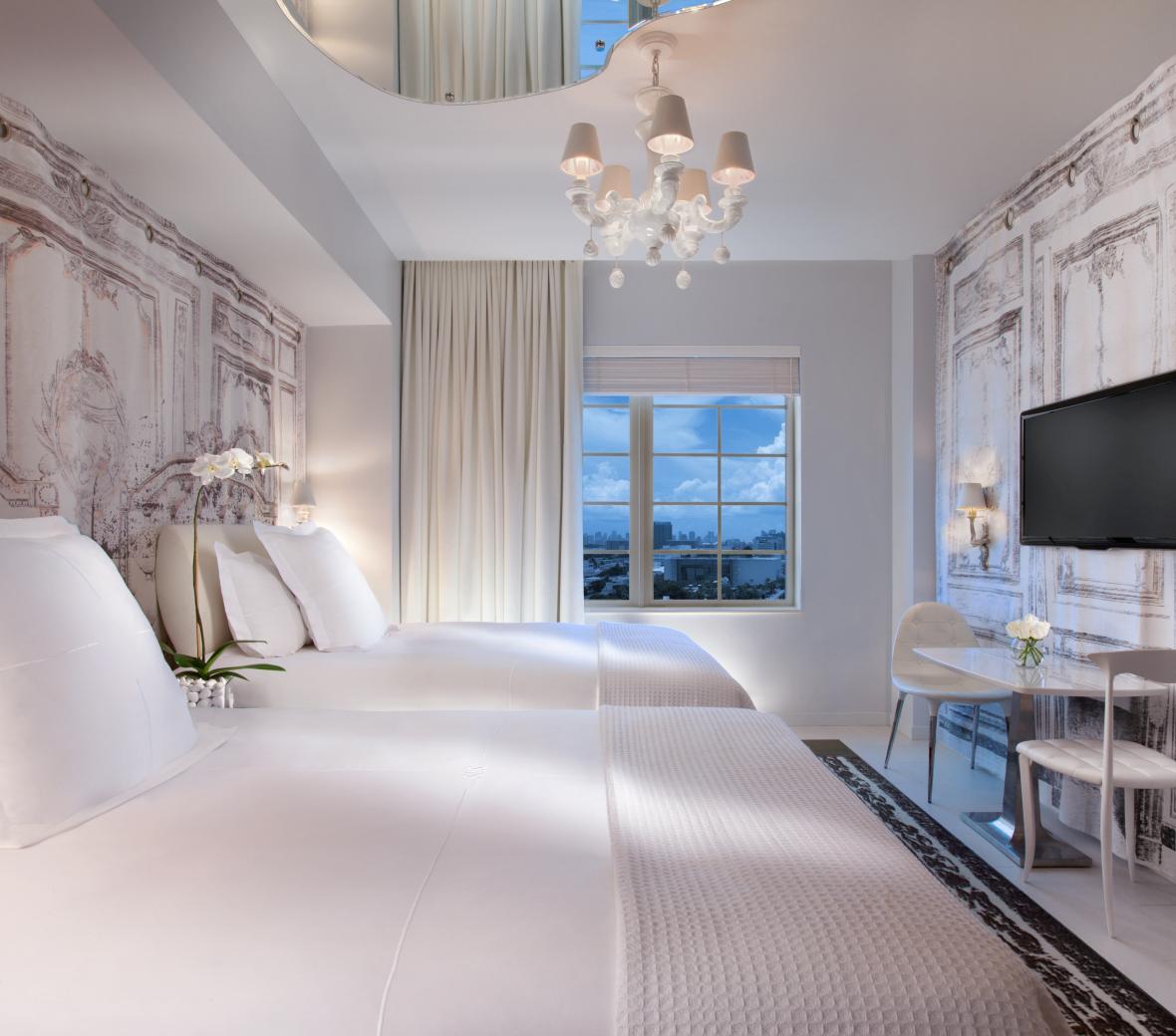 Two beds with white linens in room with white chandalier