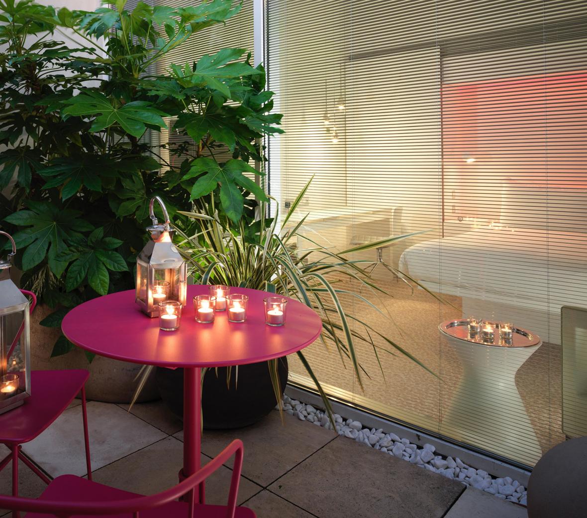 pink table and chairs with candles on balcony looking into hotel bedroom