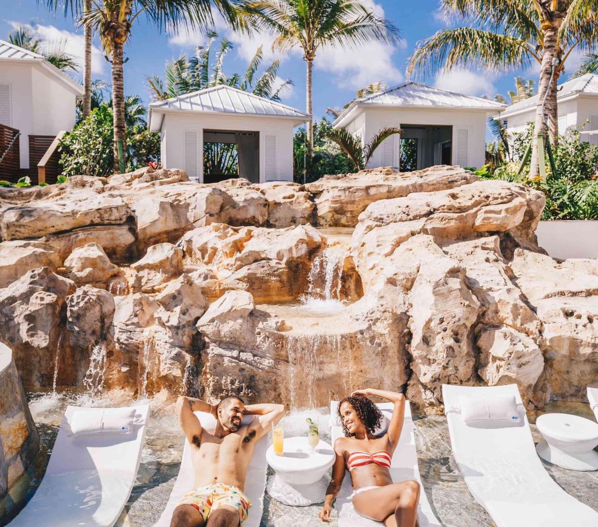 couple lounging on beach chairs with cabanas in background