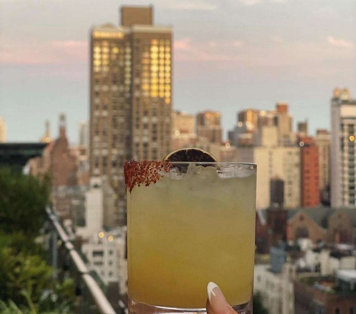 toasting a cocktail with the NY skyline behind it
