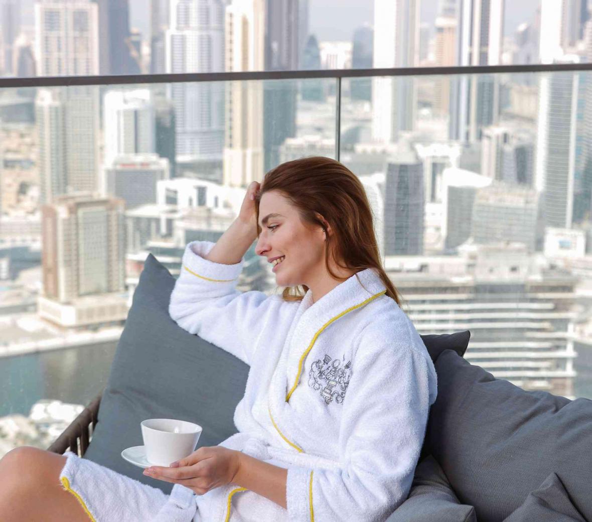 A woman sitting in a robe on her balcony drinking coffee