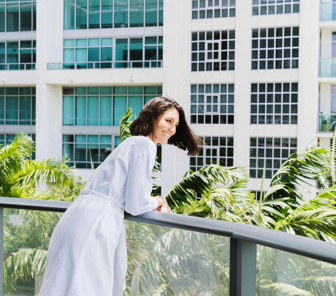 Woman in a white bathrobe looking over the hotel balcony. 