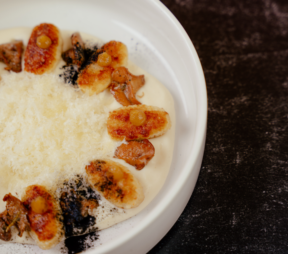 pan fried gnocchi on top of a bechamel sauce, covered with parmesan, and topped with fried chick peas
