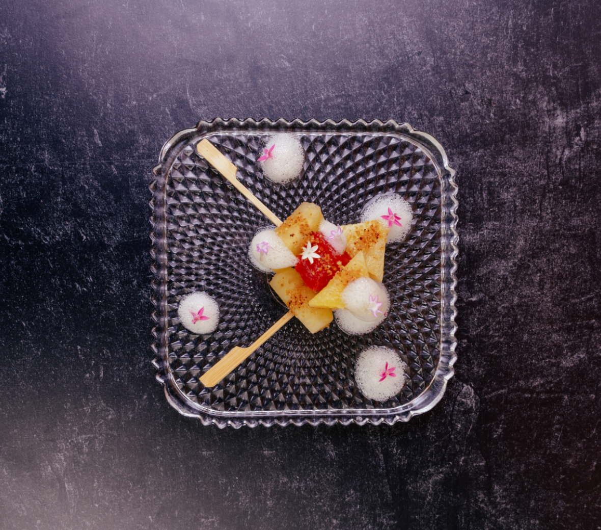 pineapple and watermelon on skewers on a clear glass plate with foam