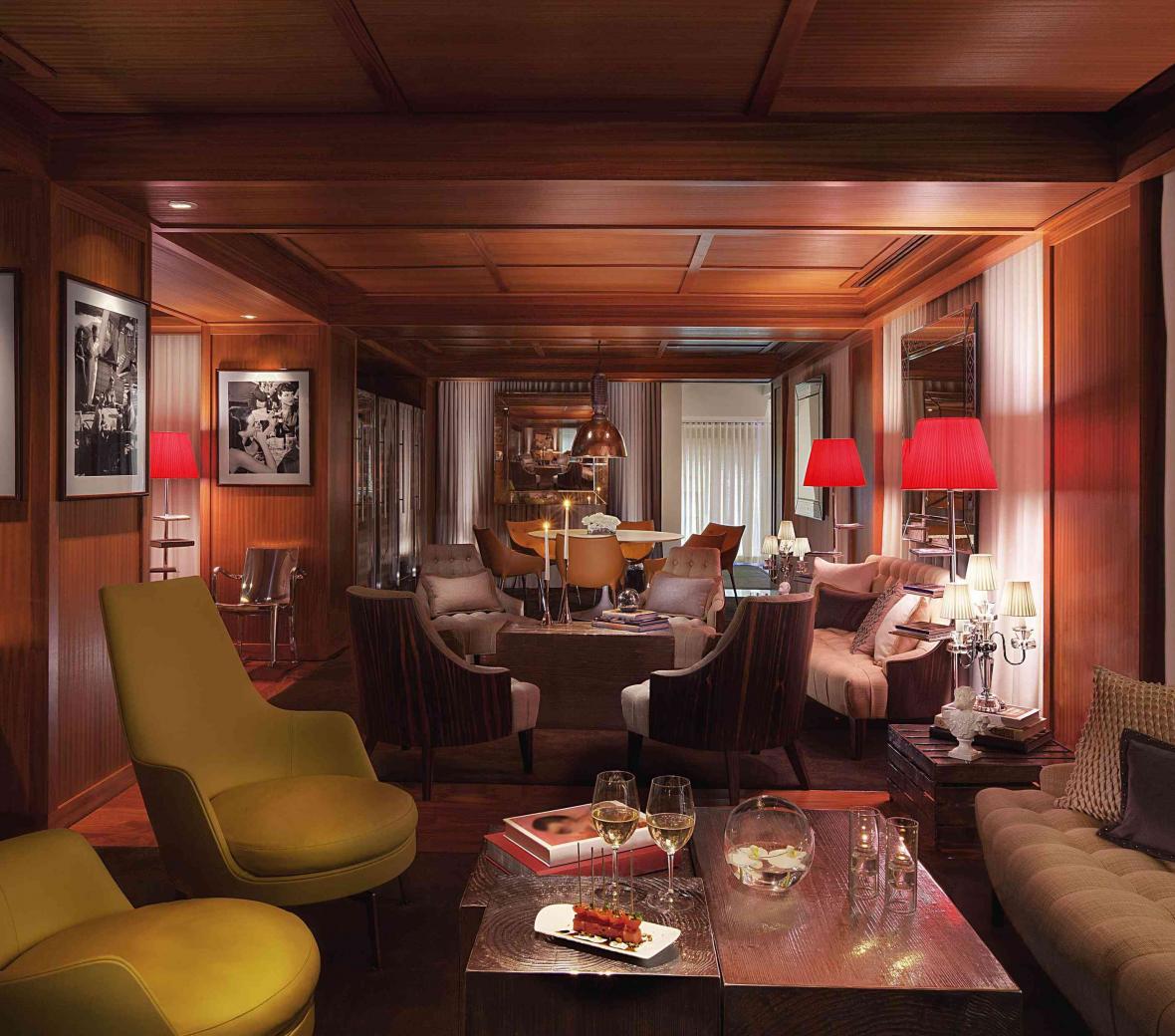 lounge area with red lamps, two olive green chairs and a coffee table with two glasses of wine