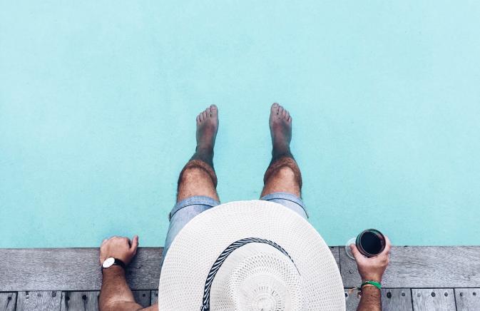 A bird-eyes view of a man sitting at a pool with a drink. 