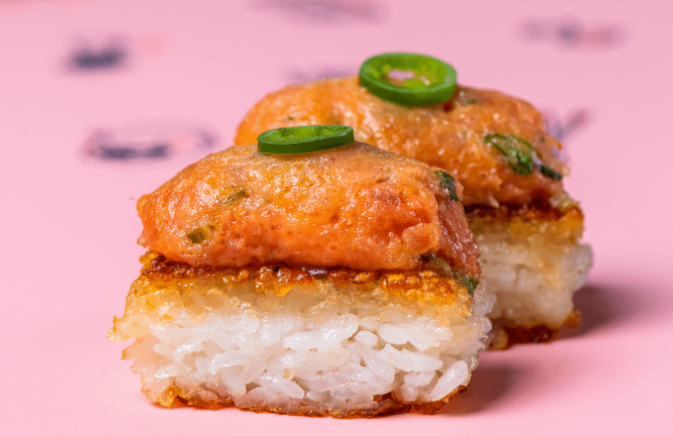 sushi with jalapenos on top sitting on pink packaging