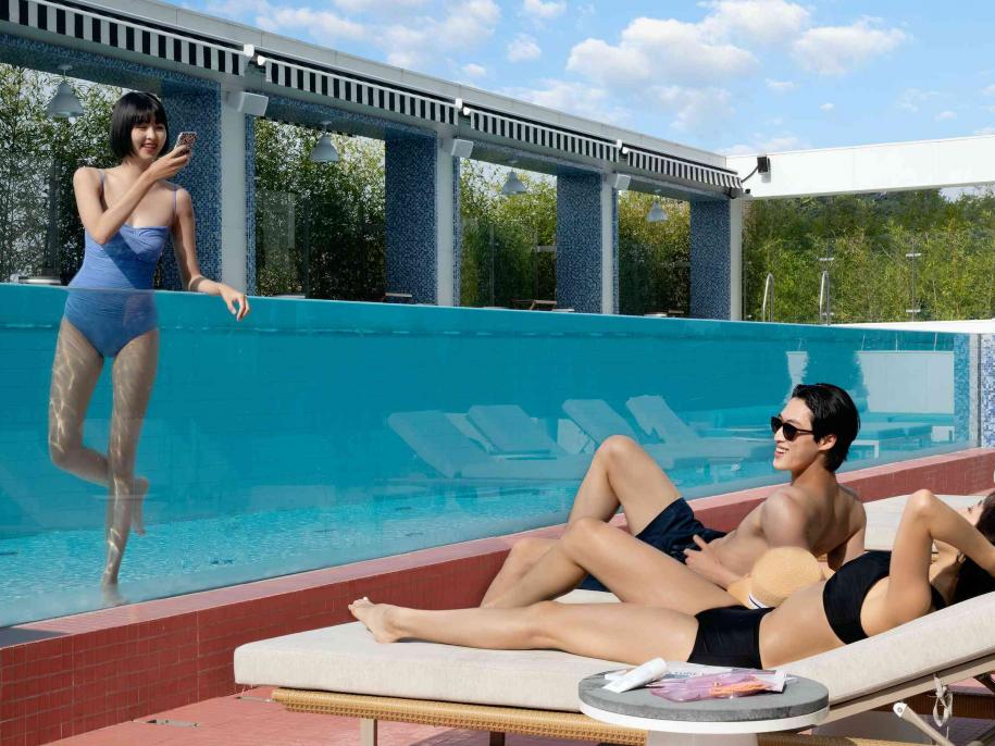 couple in loungers by a pool with a friend in the pool
