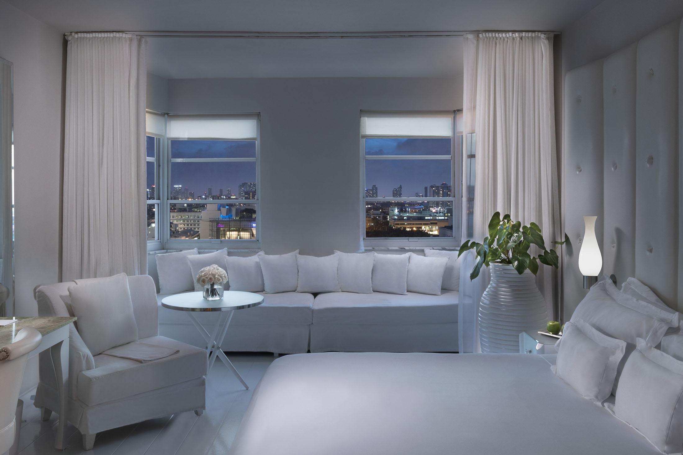 white bed and white sitting alcove in front of window with city view