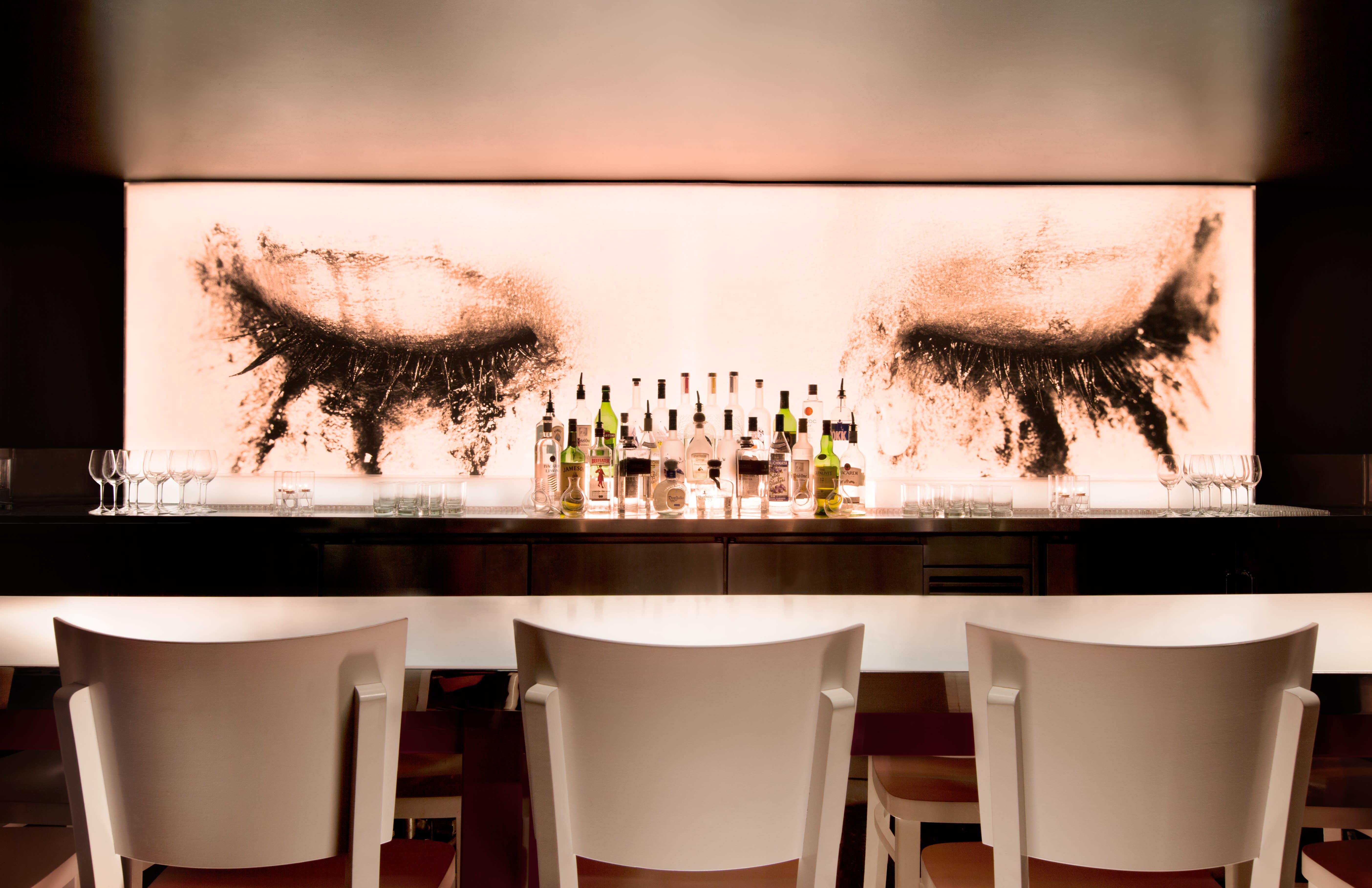bar with three white chairs with liquor display and wall mural with eyes and smudged mascara