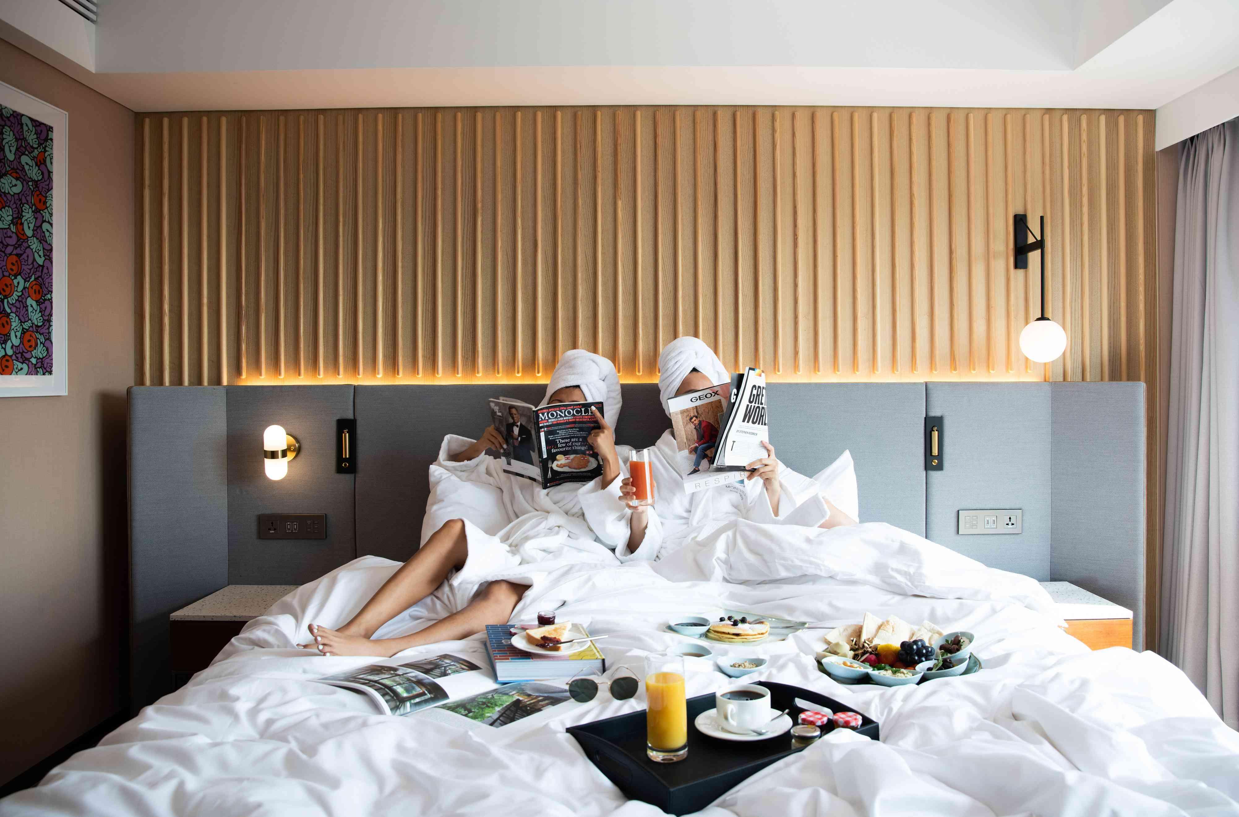 people on hotel bed with breakfast
