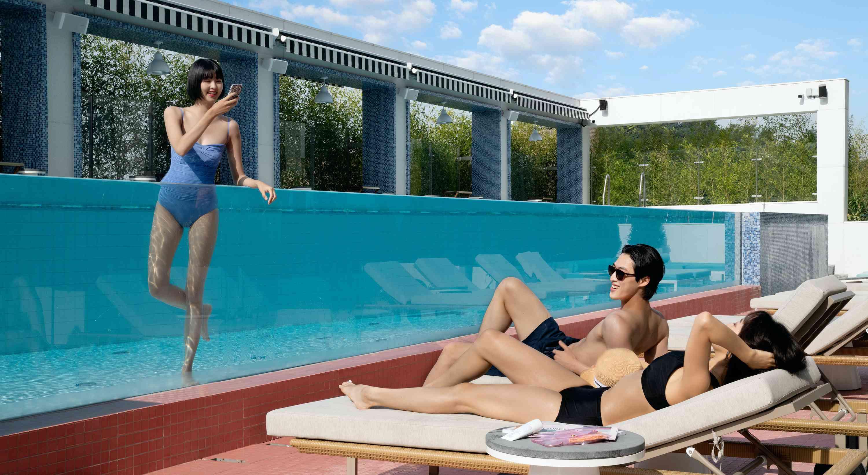 couple in loungers by a pool with a friend in the pool