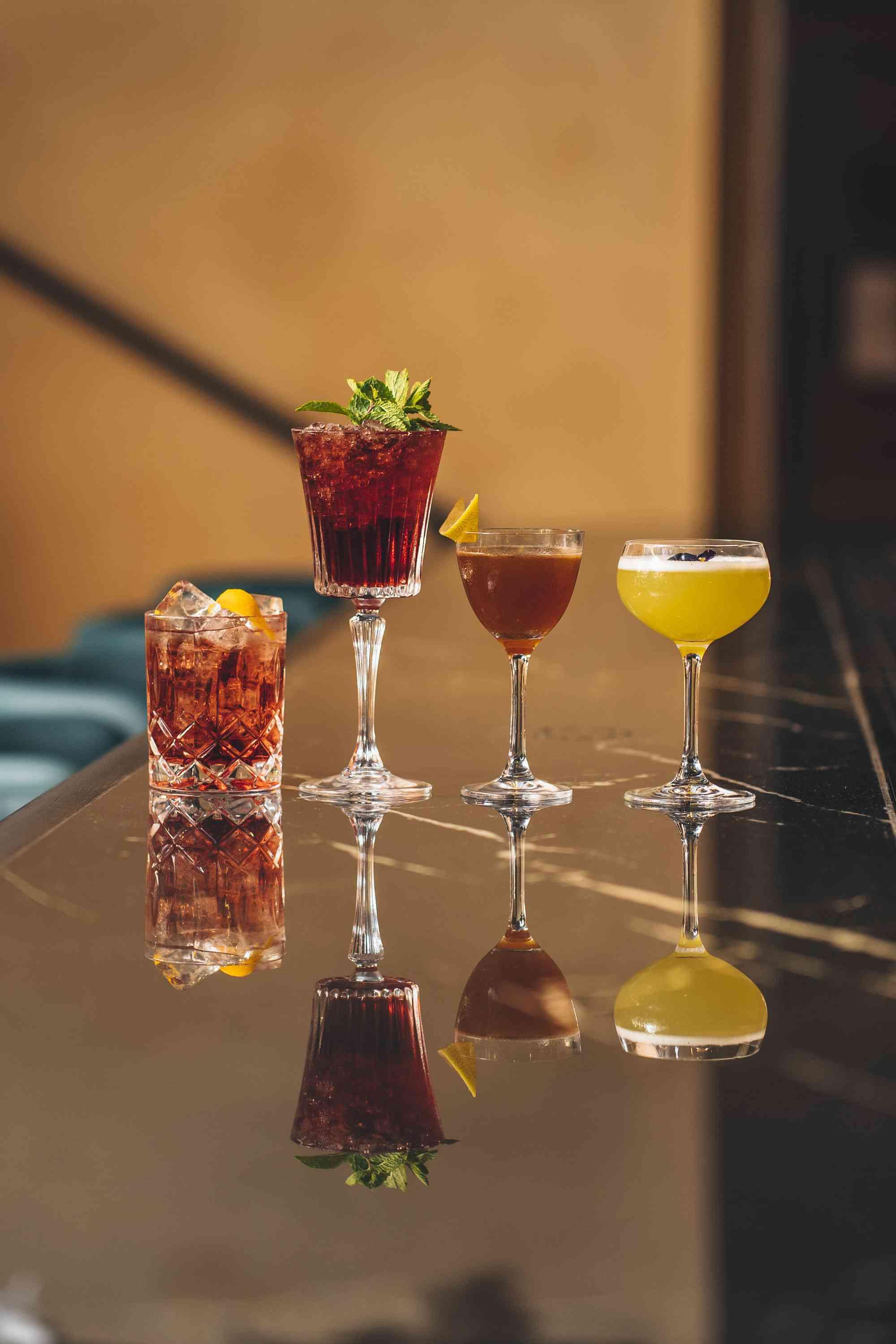 Four cocktails on a bar in various sized glasses