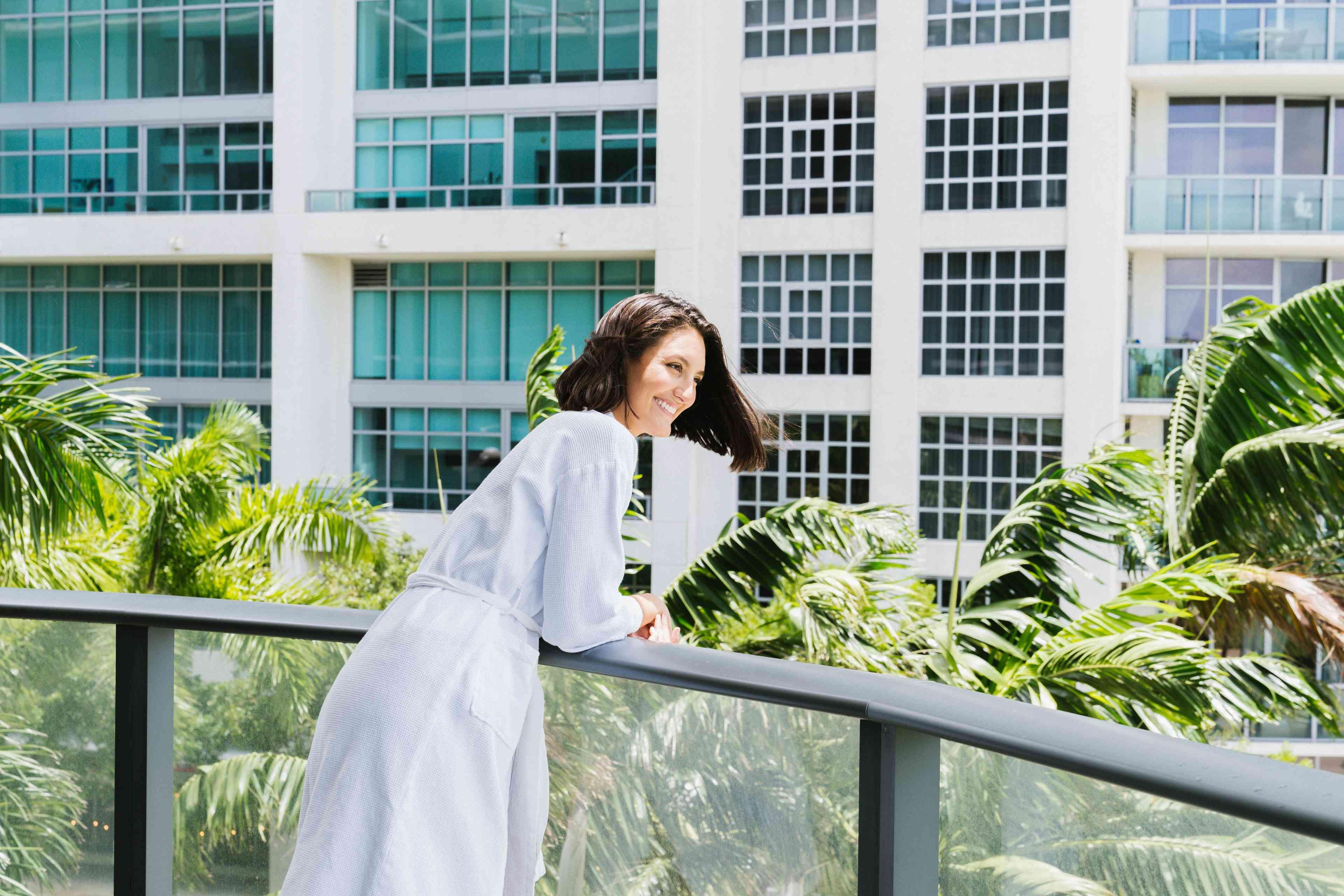 Woman in a white bathrobe looking over the hotel balcony. 