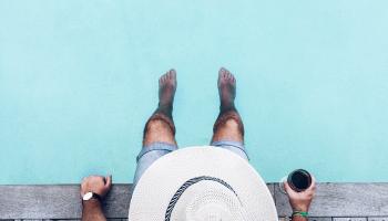 A bird-eyes view of a man sitting at a pool with a drink. 