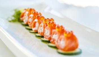Salmon sushi topped with row on a bed of cucumber.